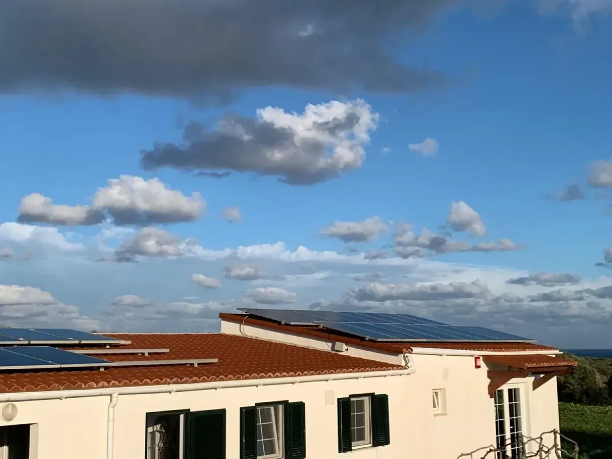 Edificio blanco con contraventanas verdes bajo un cielo azul con nubes dispersas, con vistas al mar.