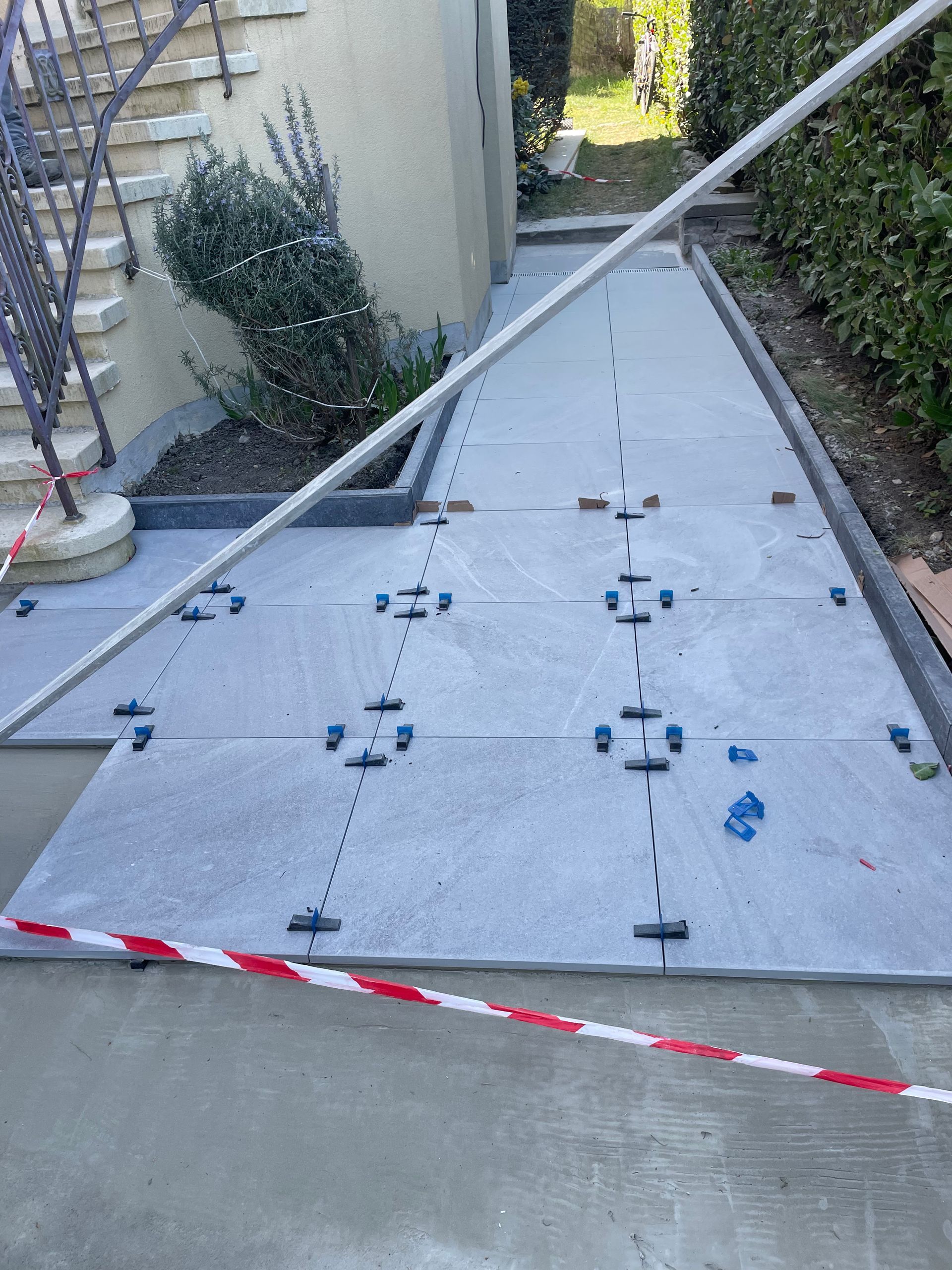 Chemin en construction, grandes dalles grises, entretoises bleues et ruban de prudence rouge/blanc.