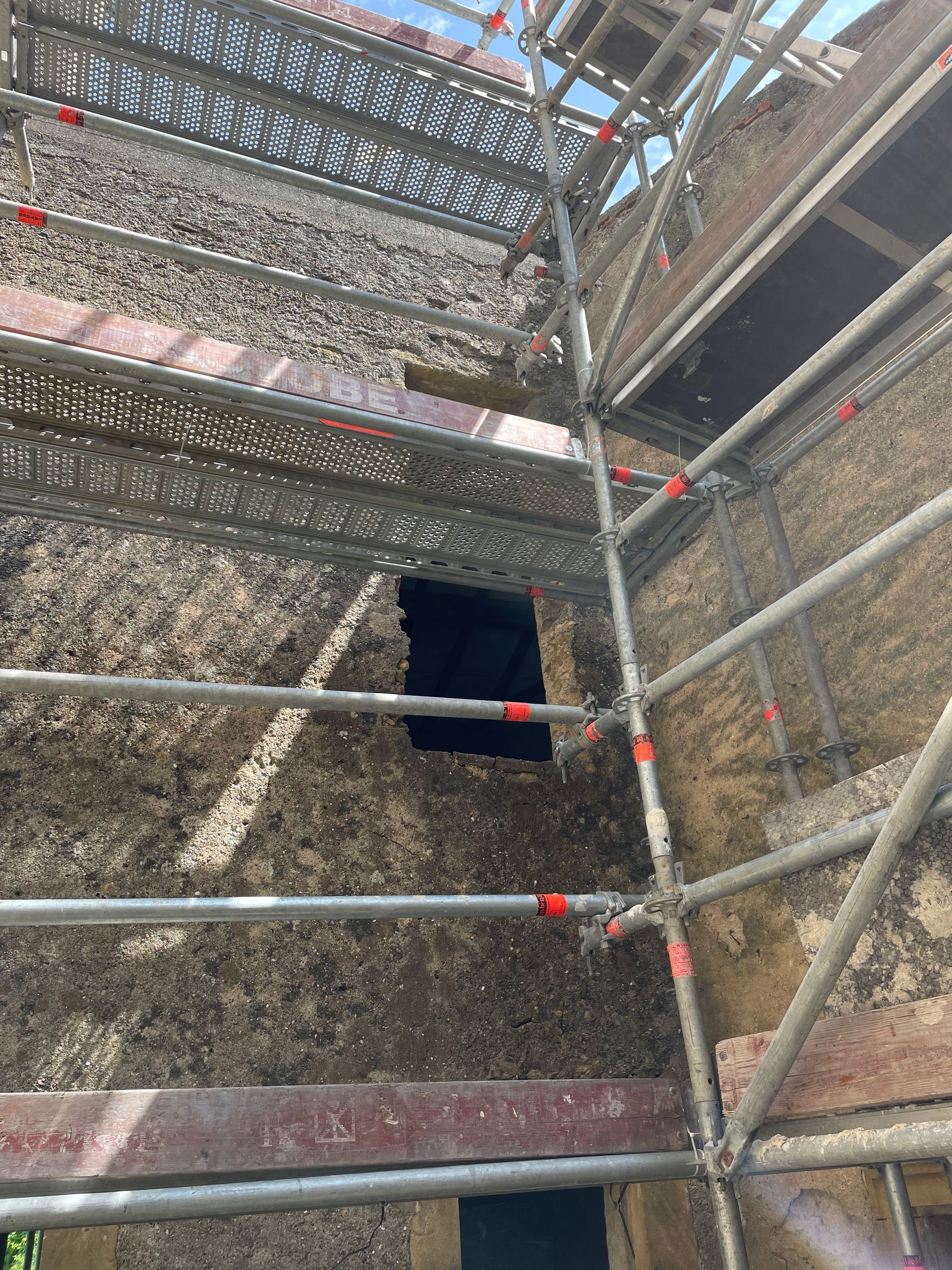 L'extérieur d'un bâtiment en ruine avec des échafaudages ; une ouverture carrée est visible.