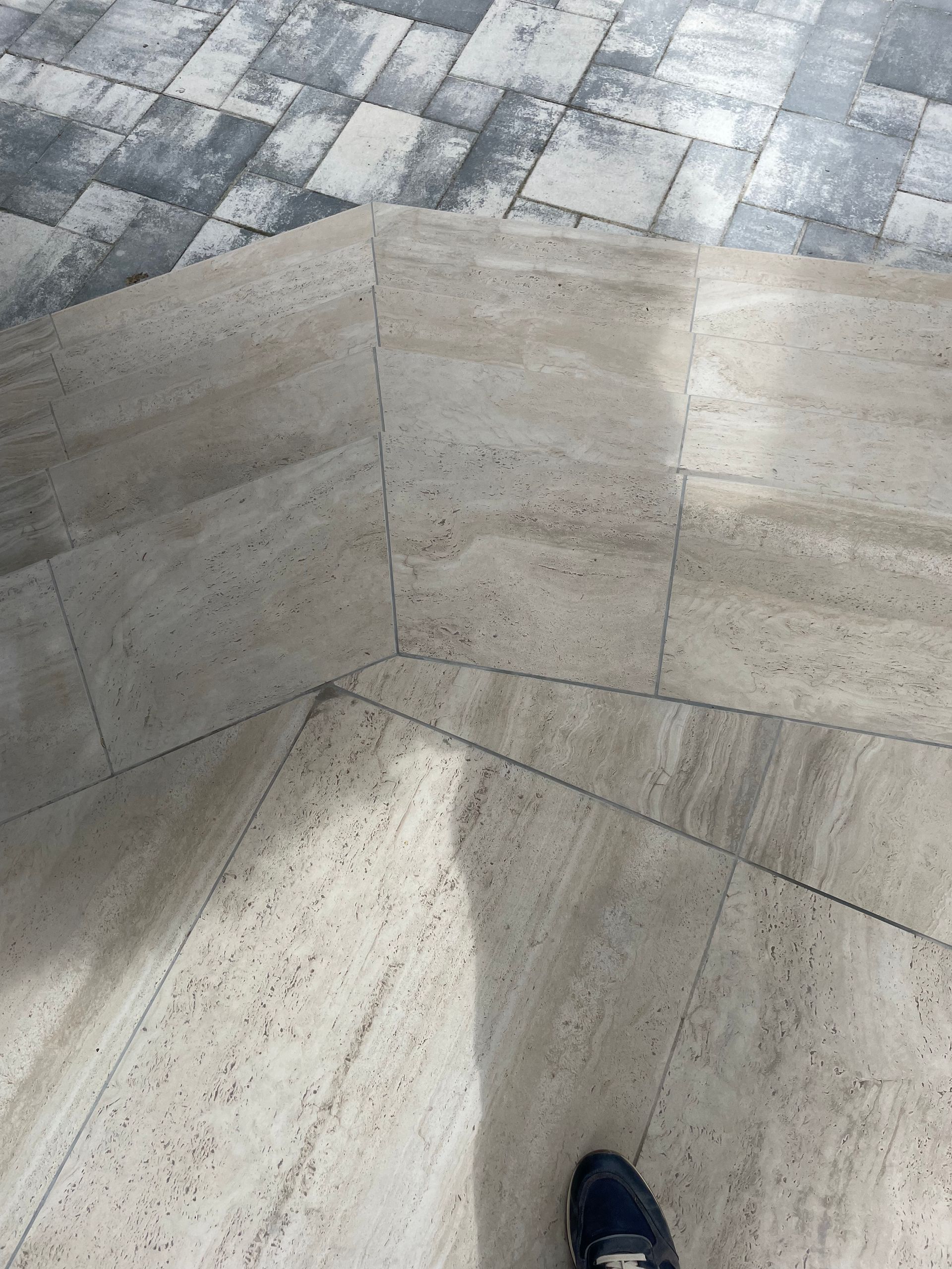 Coin de sol carrelé beige avec la chaussure d'une personne dans le coin et un trottoir à carreaux gris au-dessus.