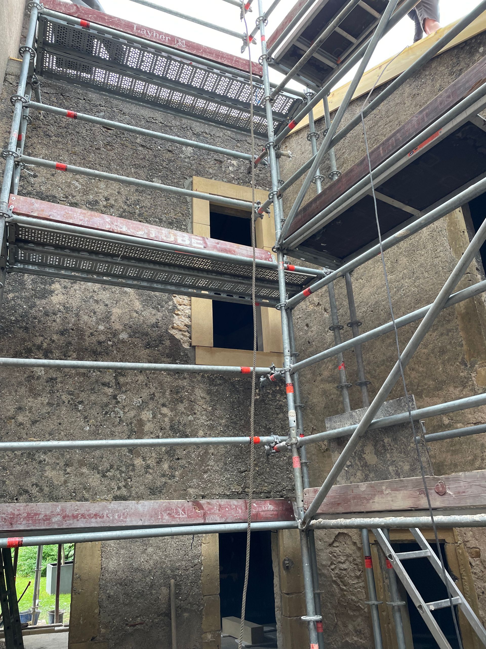 Échafaudage sur l'extérieur d'un bâtiment en pierre, fenêtres visibles, construction en cours.