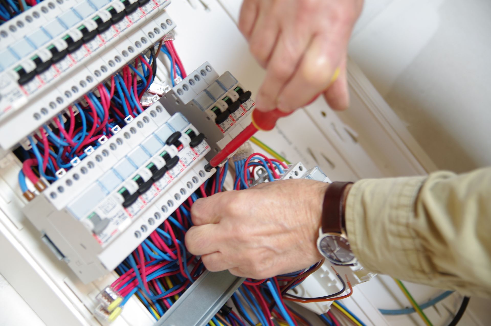 Un électricien travaille sur un tableau électrique, utilisant un tournevis pour connecter des fils.