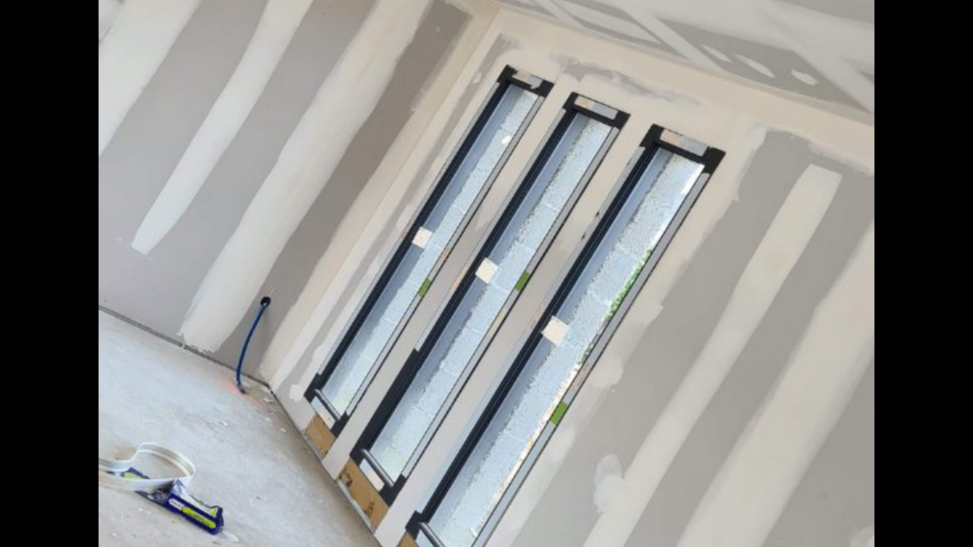 Personne portant un tablier et tenant une truelle avec de l'enduit à plaques de plâtre.