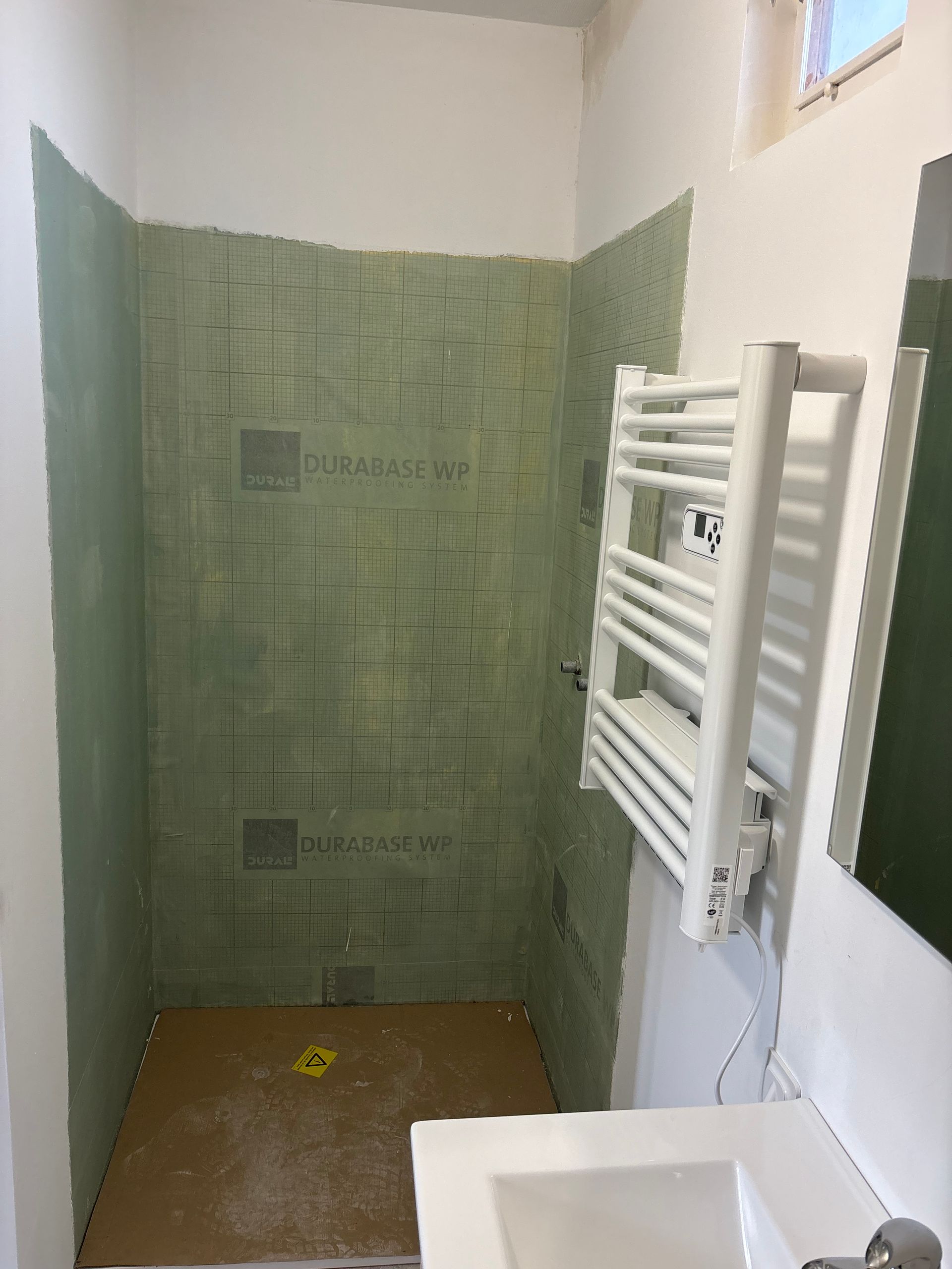 Extérieur d'un bâtiment blanc avec des volets bruns et des colonnes de porche. Un paillasson et des feuilles sont visibles.