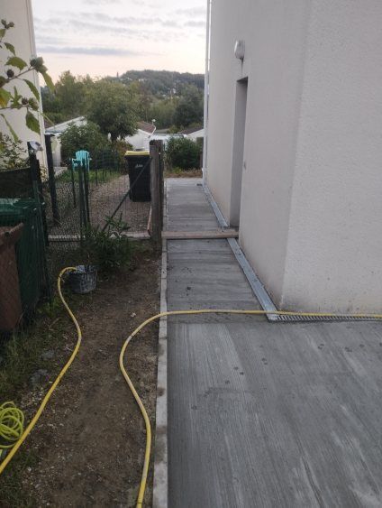 Vue aérienne d'une ville aux toits orangés, traversée par une rivière, et bordée d'arbres verts par une journée ensoleillée.