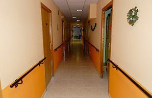 Pasillo vacío con paredes beige, molduras naranjas, pasamanos y suelo de baldosas en el corredor de un edificio