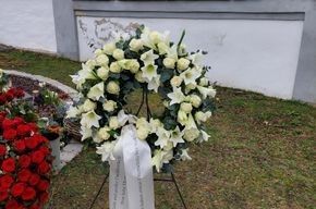 Ein Kranz aus weißen Blumen steht auf einem Ständer vor einem Gebäude.