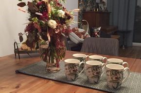 Ein Tisch mit einer Blumenvase und sechs Kaffeetassen darauf.