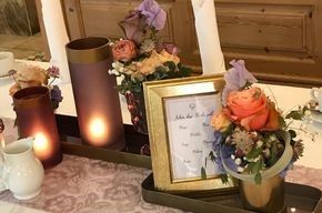Ein Tisch mit Blumen, Kerzen und einem Bilderrahmen darauf.