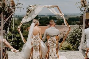 Eine Braut und ein Bräutigam sitzen bei ihrer Hochzeitszeremonie unter einem Bogen.