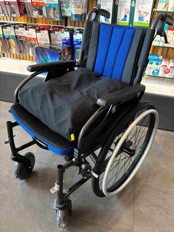 Silla de ruedas azul y negra en el pasillo de una tienda, con ruedas traseras grandes y ruedas delanteras giratorias.
