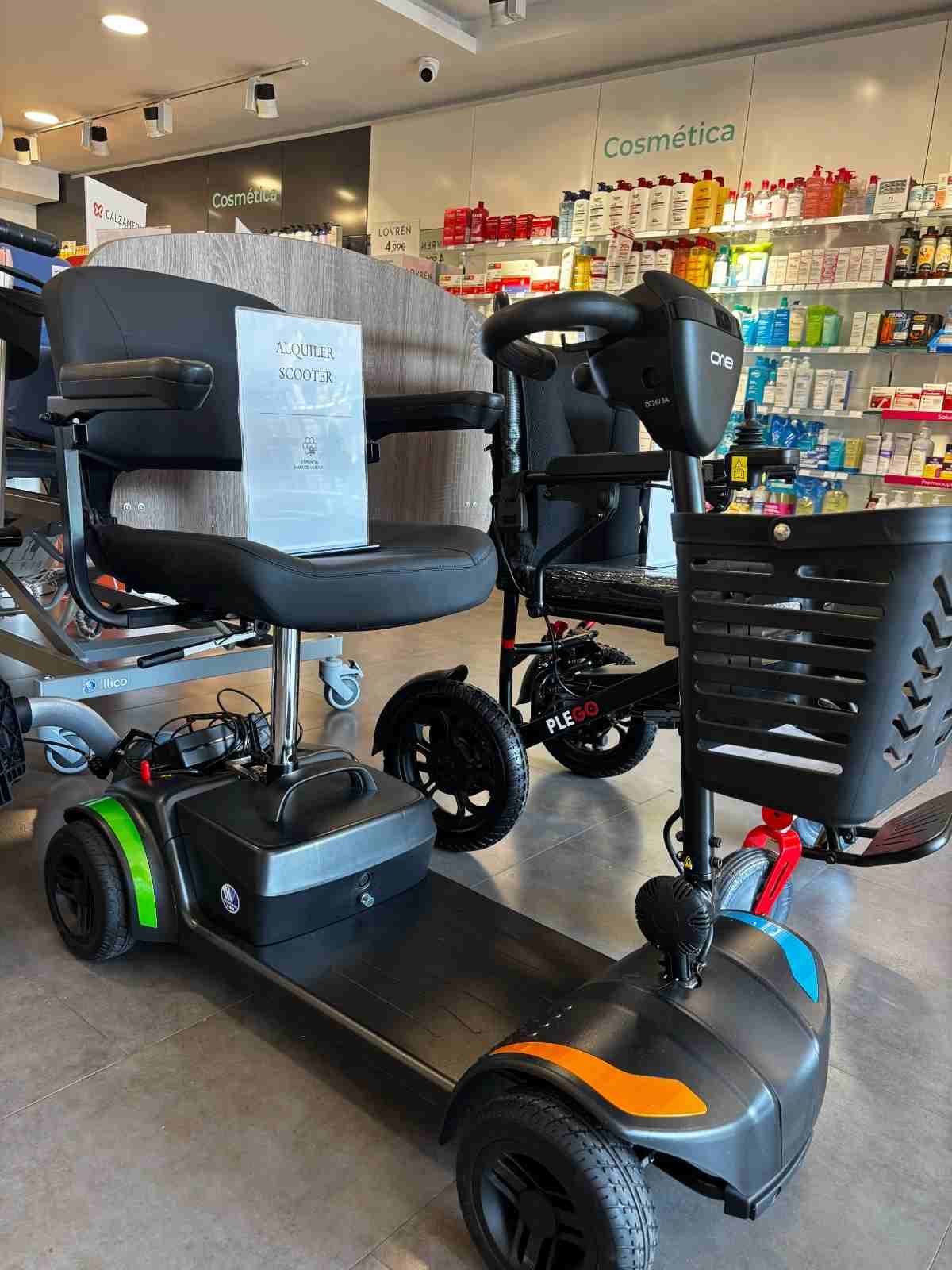 Scooter eléctrico de movilidad con asiento negro y detalles verdes expuesto en el pasillo de una tienda.