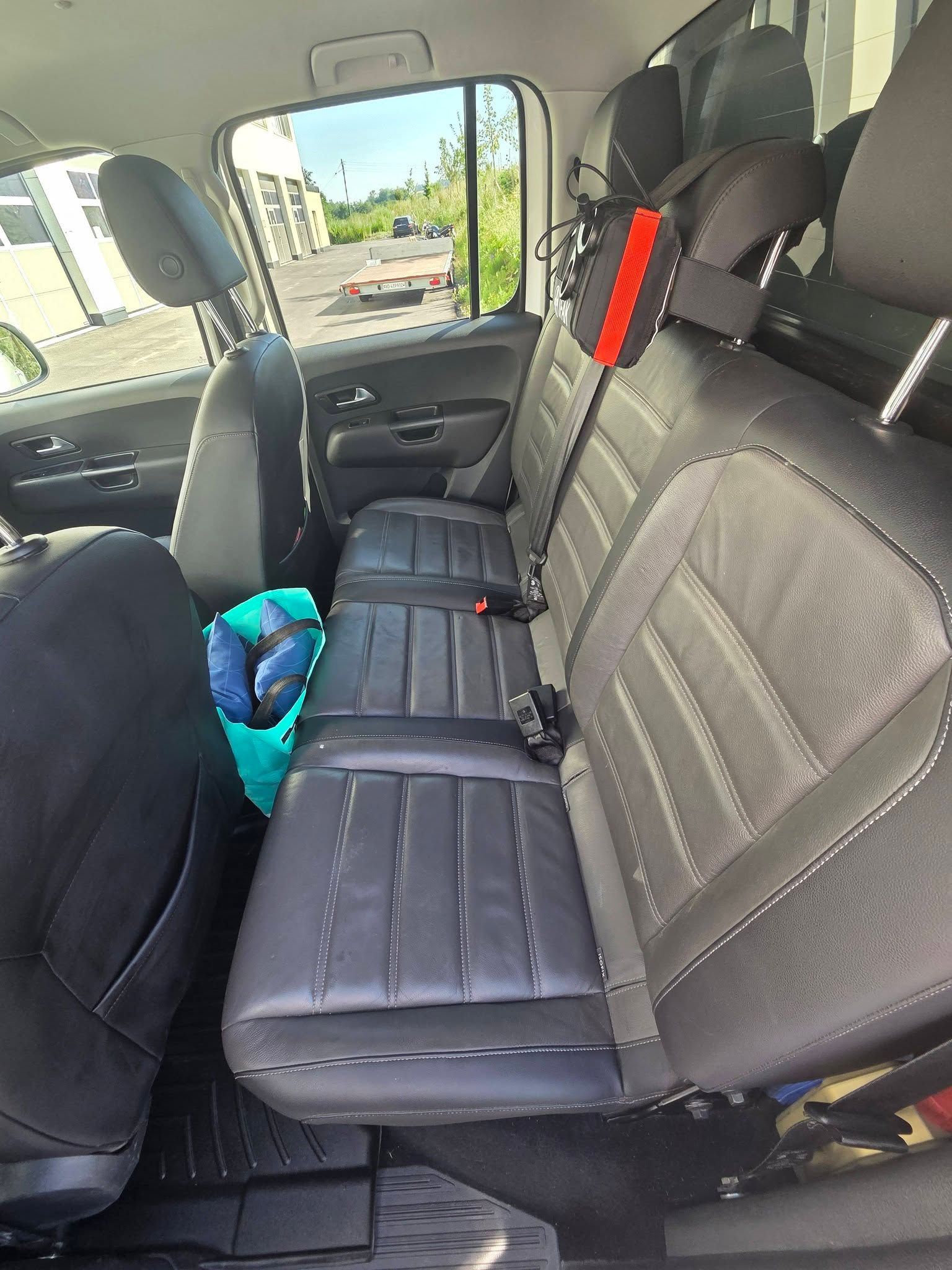 Intérieur d'une camionnette avec banquette arrière noire rabattue et ceinture de sécurité rouge vif, garée à l'extérieur.