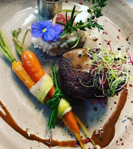 Ein Gourmetgericht bestehend aus einem angebratenen Steak, gerösteten Karotten, die mit Lauch zusammengebunden sind, einer Kugel Risotto und garniert mit Microgreens.