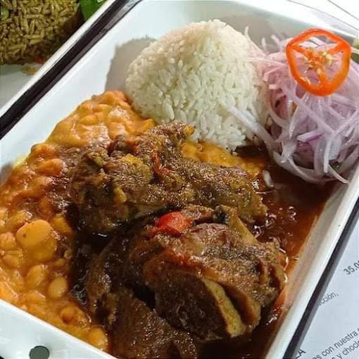 Un plato blanco cubierto con carne, frijoles, arroz y cebollas.