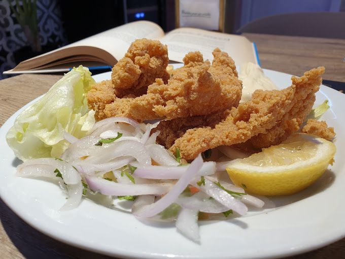 Un plato blanco cubierto con comida frita y una rodaja de limón sobre una mesa.