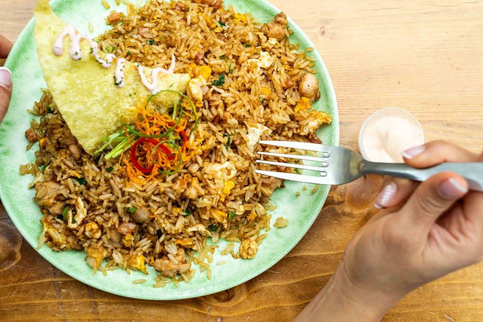 Una persona está comiendo un plato de arroz frito con un tenedor.