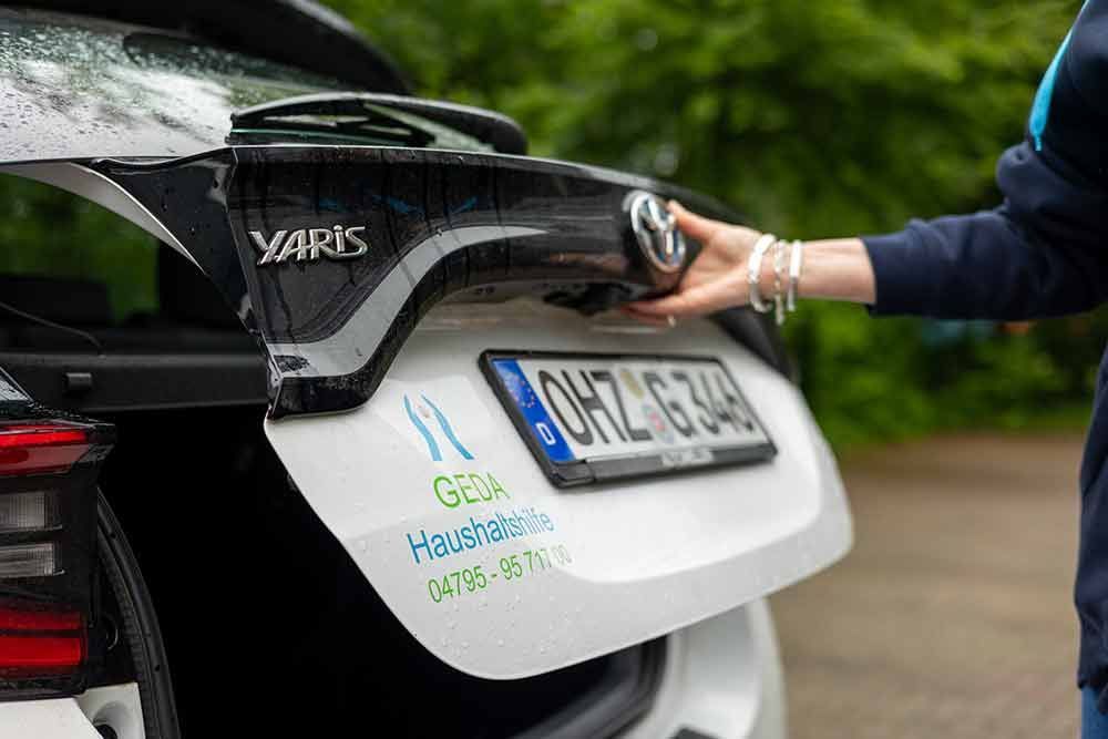 Eine Person öffnet den Kofferraum eines weißen Autos.