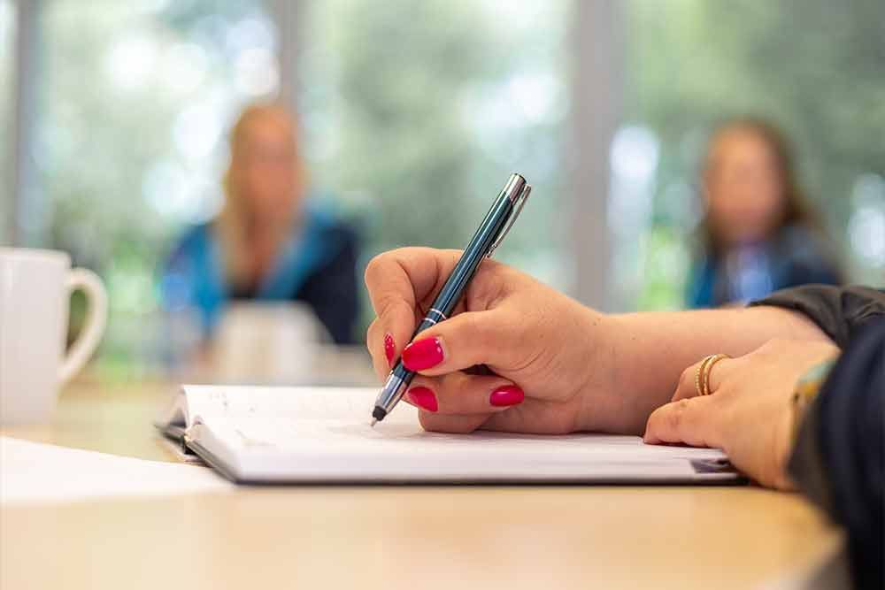 Eine Frau schreibt mit einem Stift auf ein Blatt Papier.