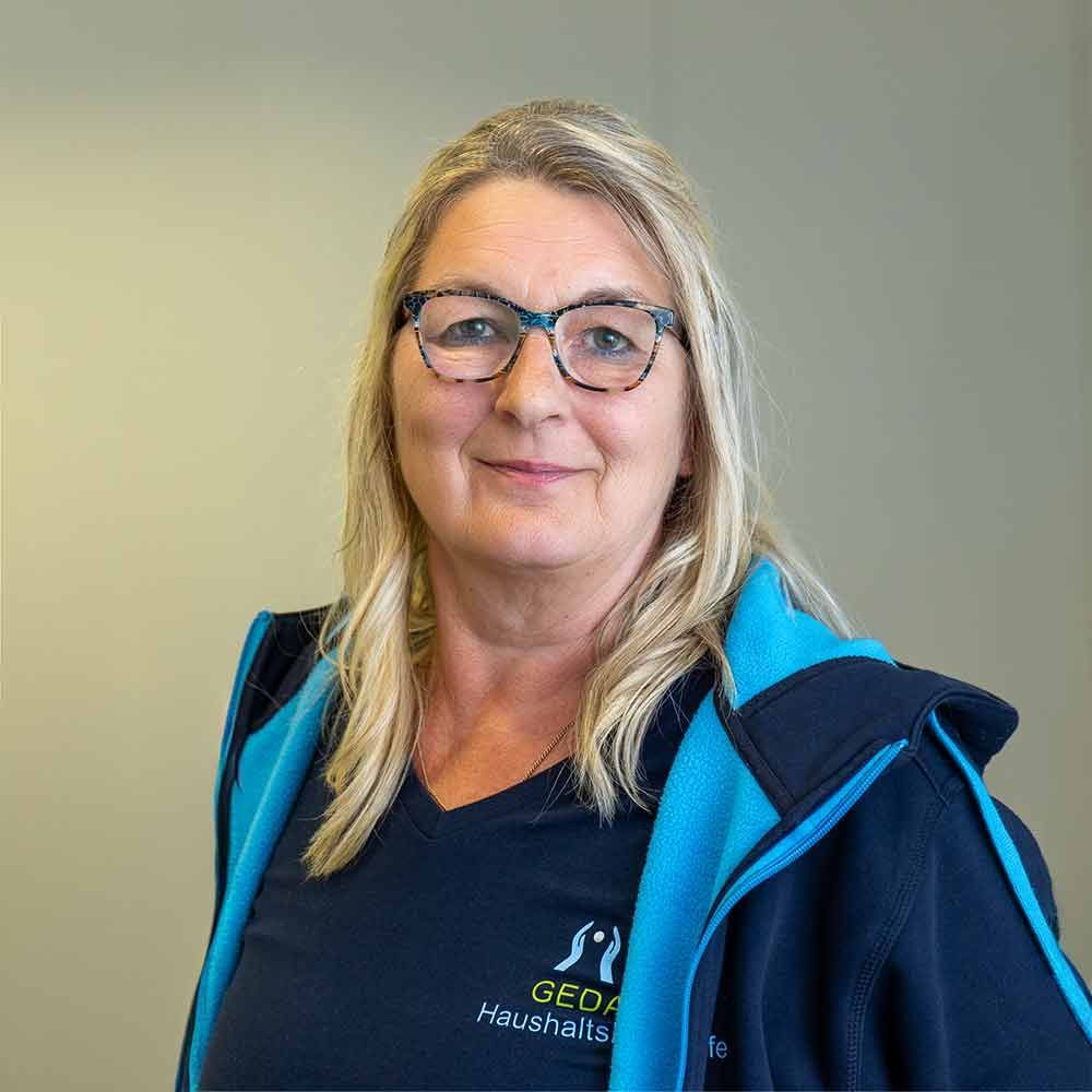 Eine Frau mit Brille und blauer Jacke lächelt in die Kamera.