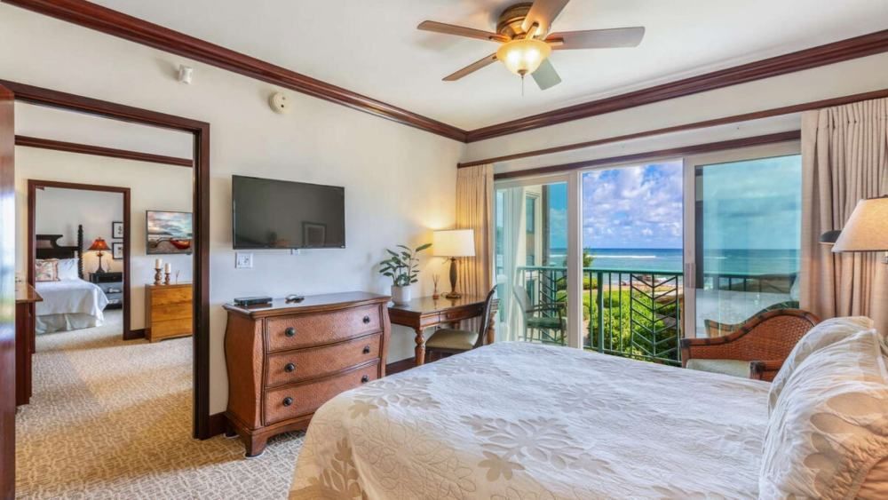 Bedroom with ocean view; bed, desk, dresser, TV, balcony, and doorway to another bedroom.