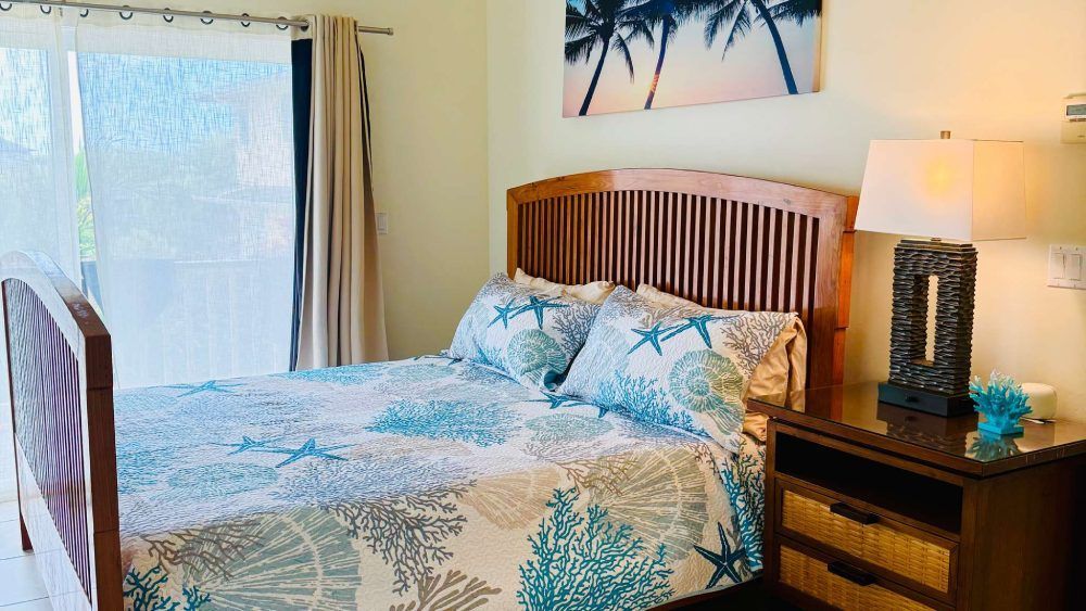 Bedroom with wooden bed, nightstand, sliding door, ocean-themed bedding, palm tree art.