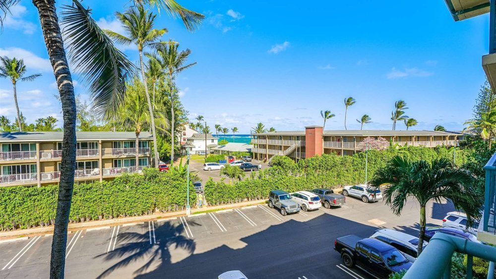 View from a balcony overlooking a parking lot, buildings, and the ocean under a bright blue sky.