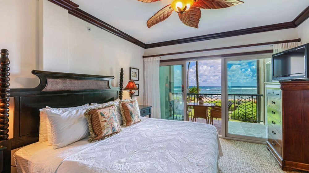 Bedroom with a four-poster bed, chest of drawers, and balcony overlooking ocean view.