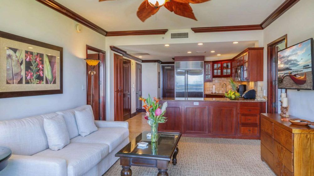 Living room with open kitchen; white sofa, wooden cabinets, view of ocean.