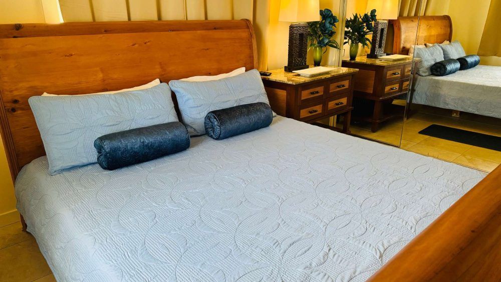 Bedroom with wooden bed frame, light blue bedding, and dark blue bolster pillows.