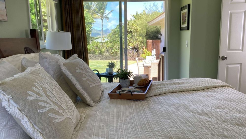 Bedroom with bed, pillows, and a tray. Sliding glass door opens to a yard with plants.