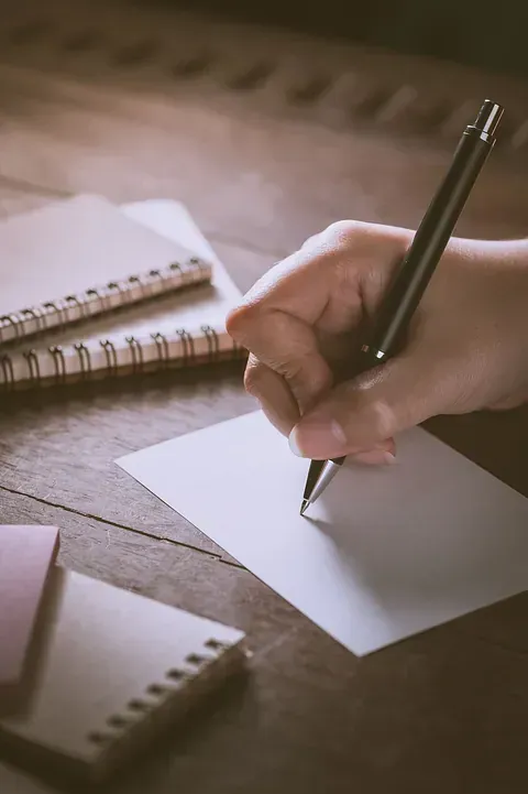 Una persona está escribiendo en un trozo de papel con un bolígrafo.