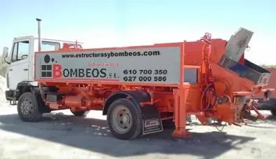 Un camión rojo y blanco con una bomba en la parte trasera está estacionado en un lote de tierra.
