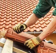 Persona con guantes de trabajo instalando una teja marrón en un techo inclinado.