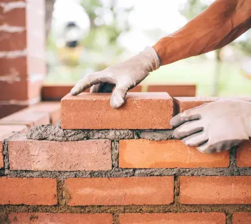 Manos en guantes colocando ladrillos con mortero.