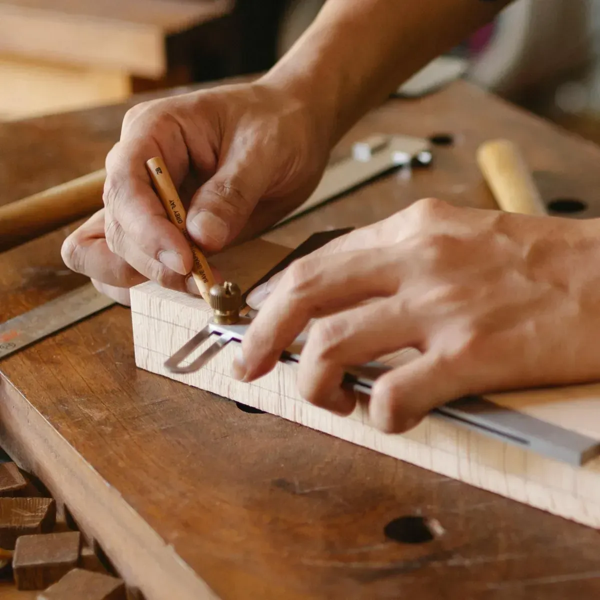 Manos de un carpintero utilizando un calibre para marcar una línea en un bloque de madera.