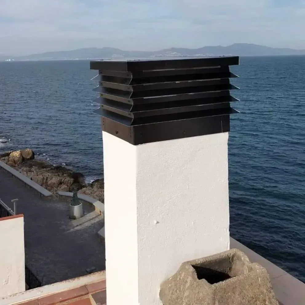 Remate de chimenea negro sobre estructura blanca con vistas al océano.