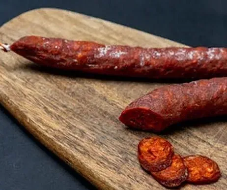 Primer pla d'un xoriço sobre una taula de tallar de fusta. Un està tallat a rodanxes, deixant al descobert la carn vermella.