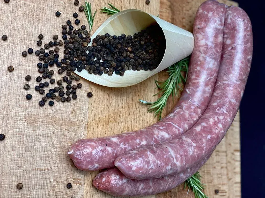 Salsitxes sobre taula de fusta amb grans de pebre i branquetes de romaní.