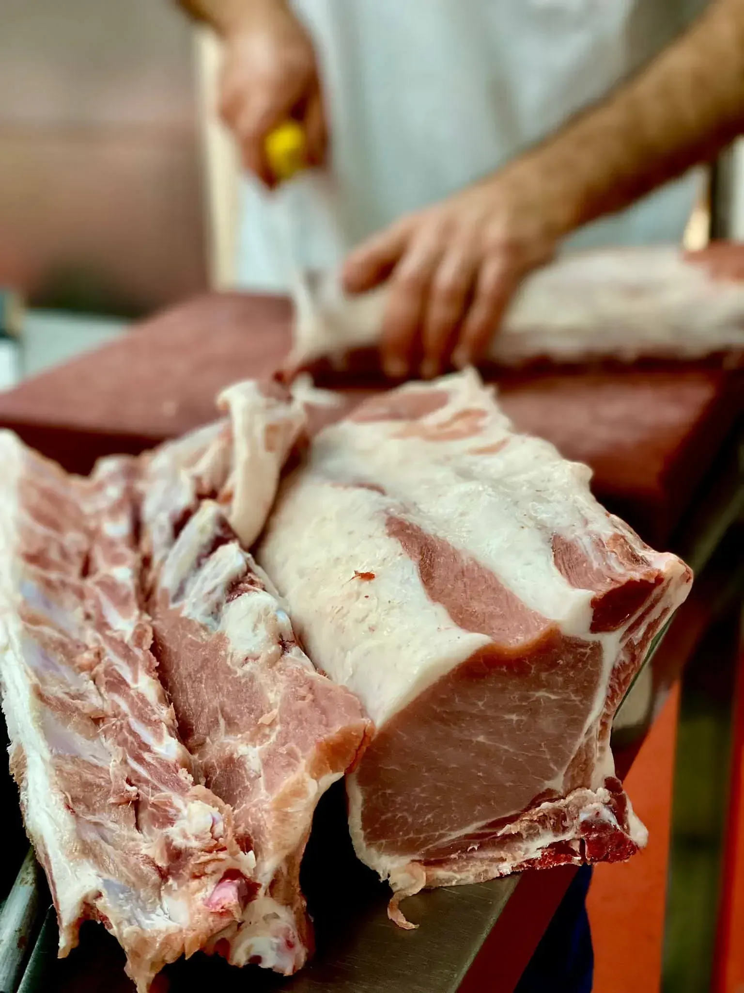 Carnisser tallant carn de porc crua en una taula de tallar vermella, amb les mans i un ganivet visibles.