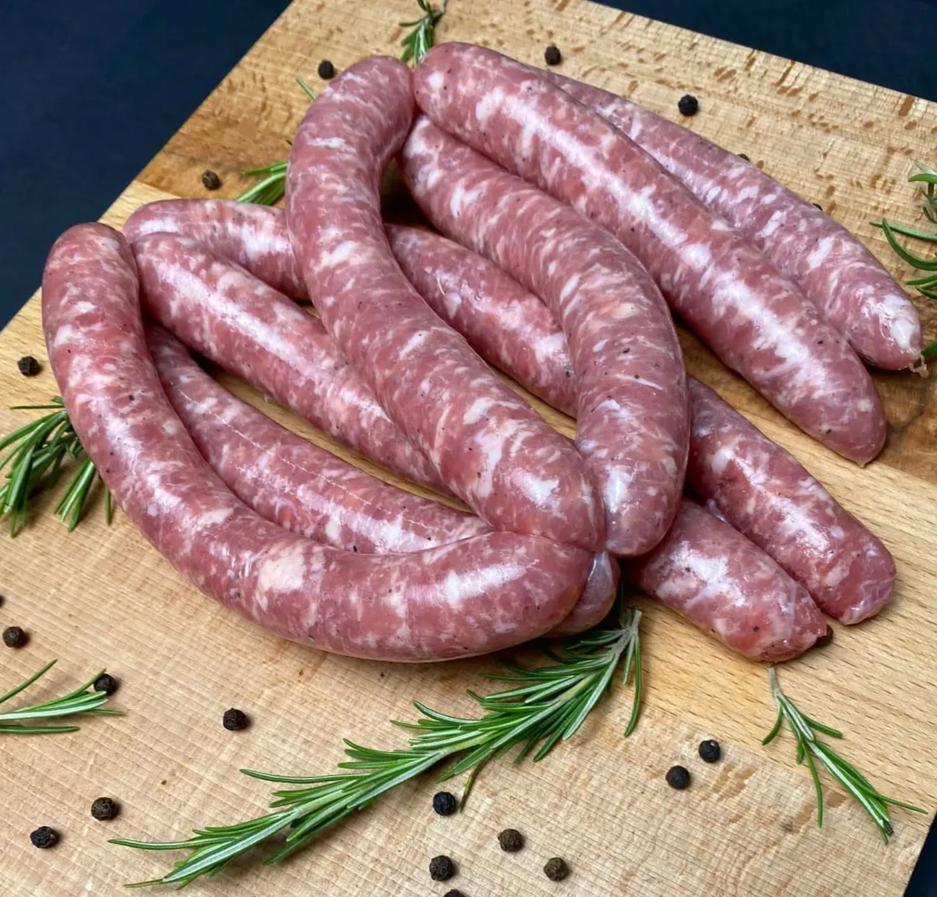 Salsitxes crues sobre una taula de fusta amb romaní i grans de pebre.