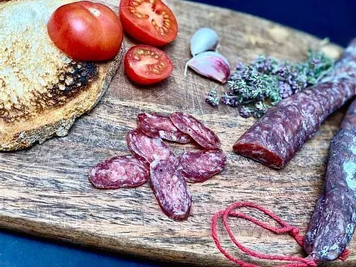 Taula de fusta amb pa, tomàquets, all, herbes i botifarra tallada a rodanxes.