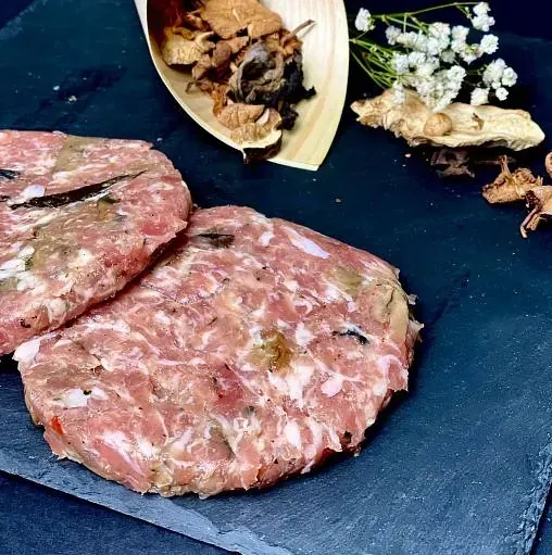 Dues llesques de terrina de carn, xampinyons, herbes i una cullera de fusta sobre una pissarra fosca.