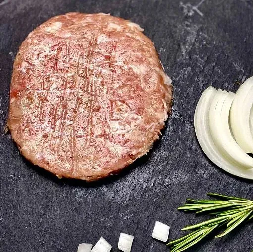 Hamburguesa crua amb rodanxes de ceba, ceba tallada a daus i branqueta de romaní sobre una superfície fosca.