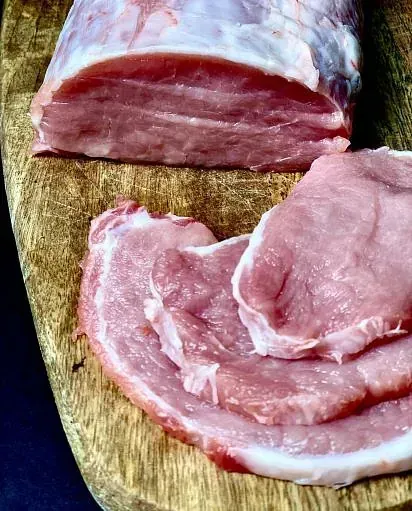Llom de porc cru amb porcions tallades sobre una taula de tallar de fusta.