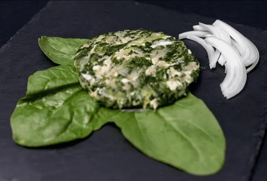Hamburguesa d'espinacs i ceba sobre fulles d'espinacs amb rodanxes de ceba, en un plat de pissarra.