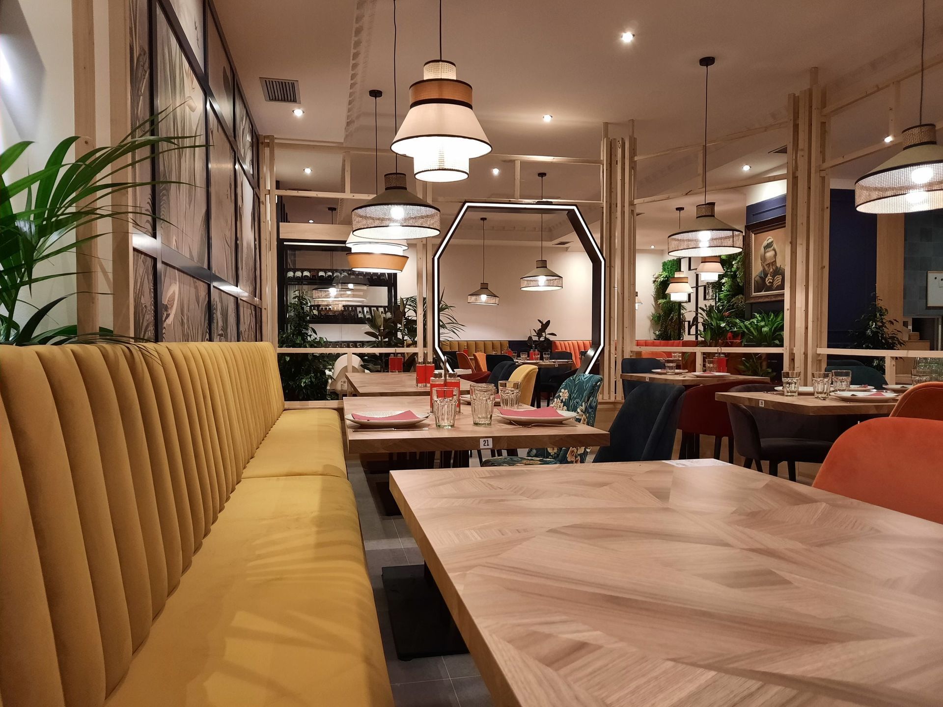 Un moderno comedor de restaurante con bancos de color amarillo mostaza, mesas de madera y lámparas colgantes.