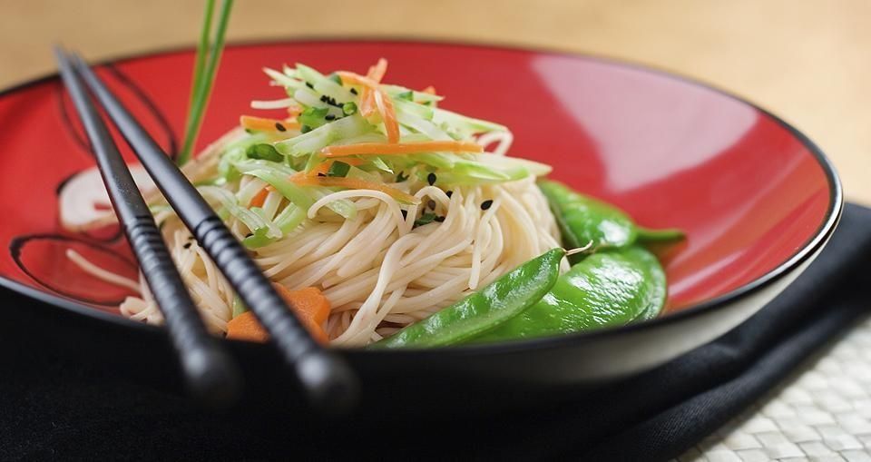 Un plato de fideos fríos cubierto con pepino y zanahorias ralladas, servido con guisantes y palillos negros.