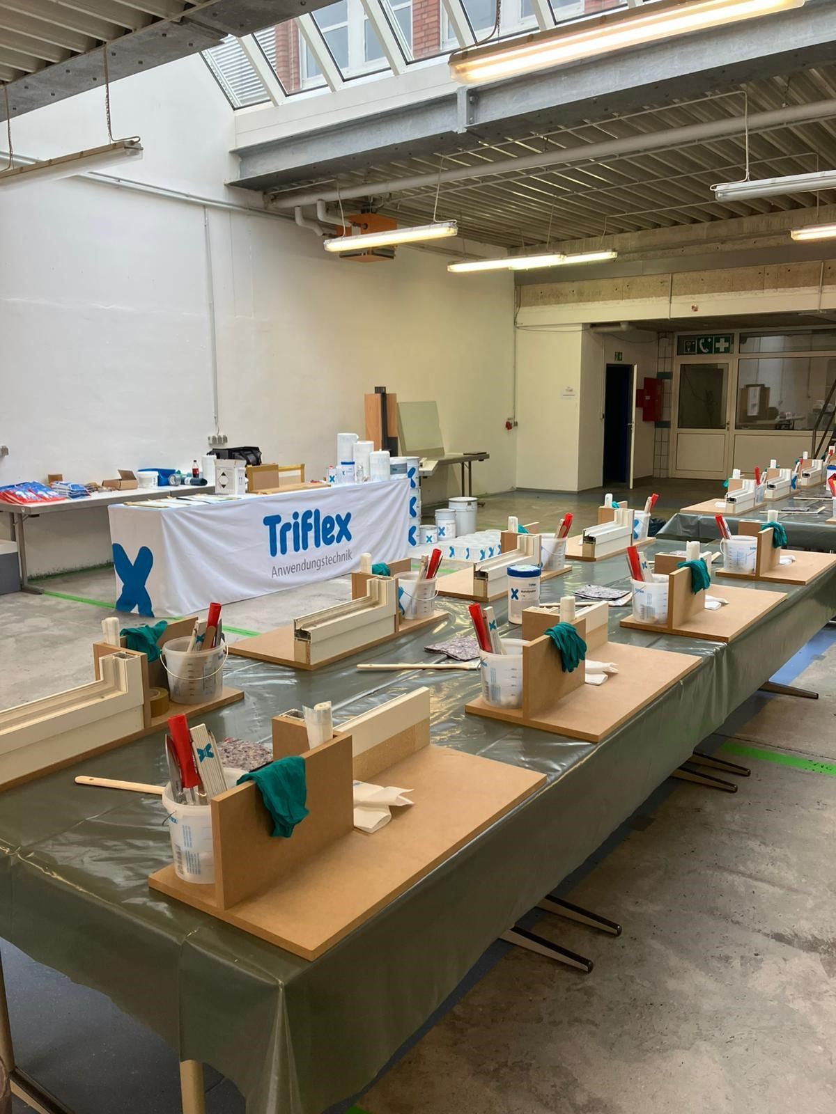 Langer Tisch für einen Triflex-Schulungsworkshop, an dem Materialien und Werkzeuge für die Teilnehmer bereitstehen.
