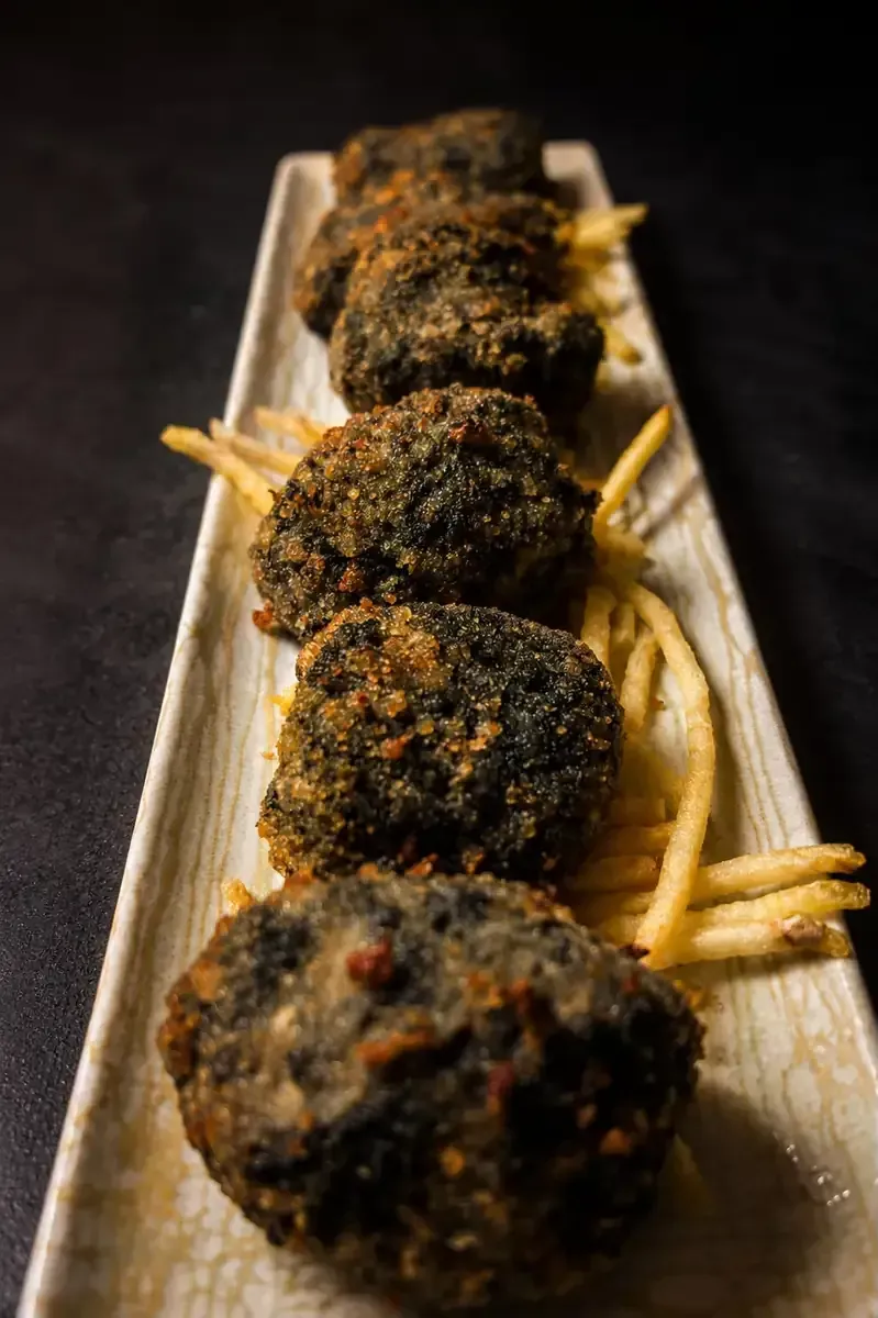 Albóndigas chamuscadas ensartadas en brochetas sobre papas fritas en una tabla de madera.